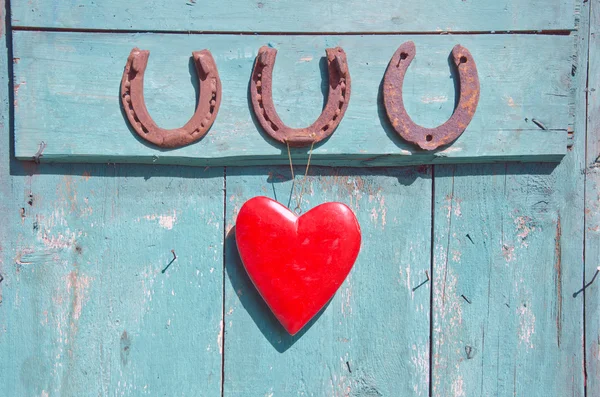 Drei alte rostige Hufeisen als Glückssymbol und rotes Herz an der Tür — Stockfoto