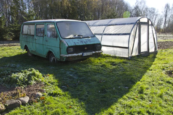 Viejo coche abandonado y invernadero de plástico en la granja — Foto de Stock