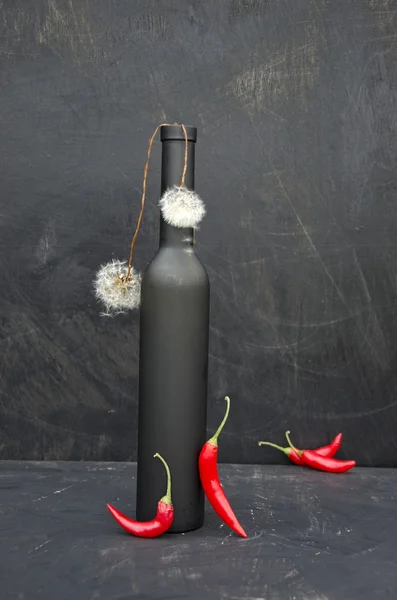 Bodegón negro con botella, chiles rojos y diente de león — Foto de Stock