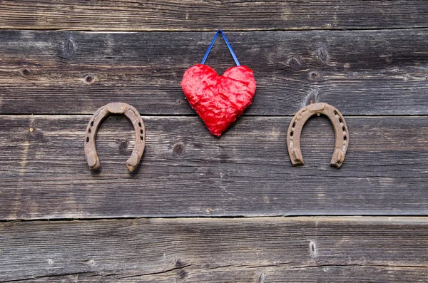 Dos símbolos de la suerte herradura oxidada y corazón de tela roja en la pared —  Fotos de Stock