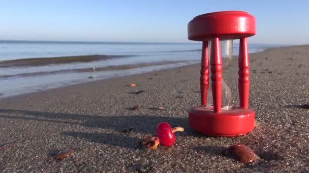 Oude rode gebroken zandloper sandglass klok en rose heupen op zee strand zand — Stockvideo