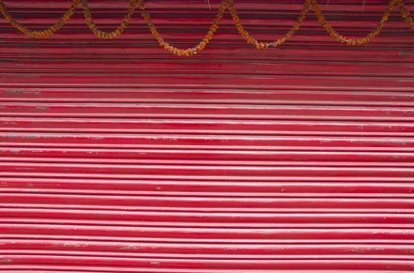 Red painted corrugated metal door and flowers garland — Stock Photo, Image