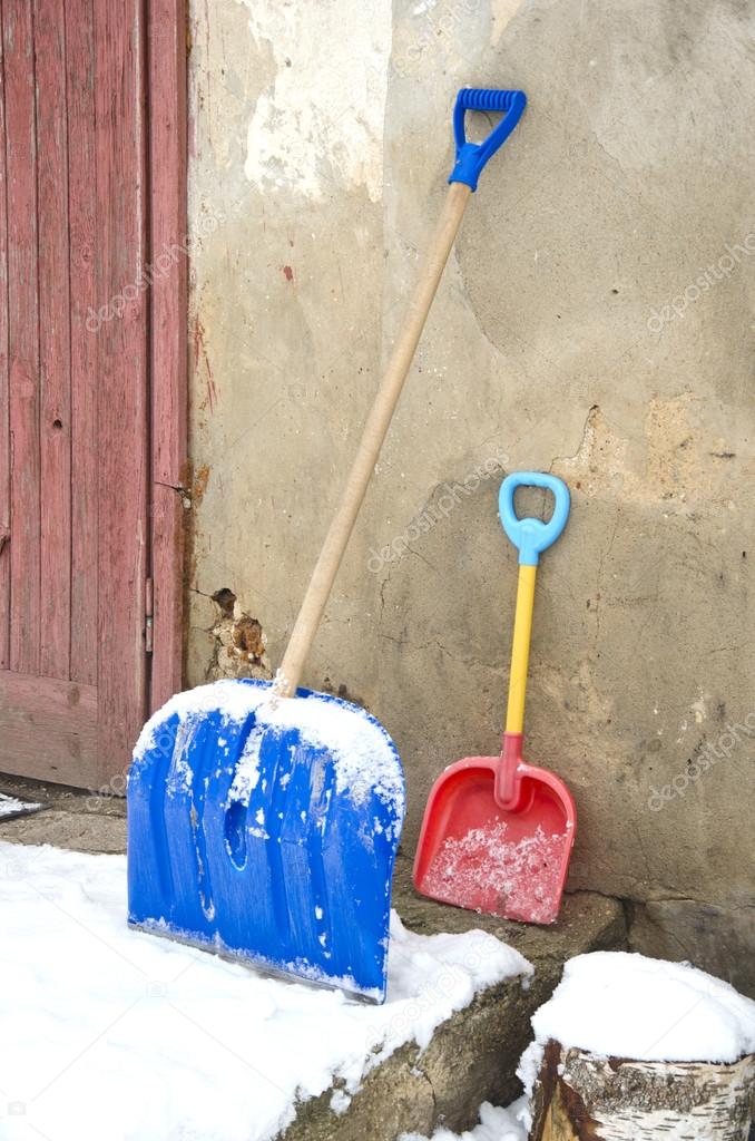 big and small father and child snow shovels near wall