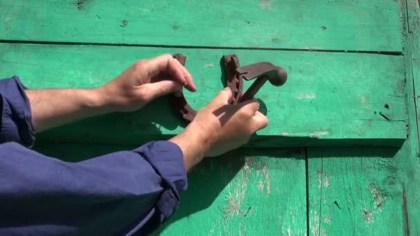 Mann hämmert Hand in Hand rostiges Hufeisensymbol des Glücks auf alte grüne Hoftür — Stockvideo