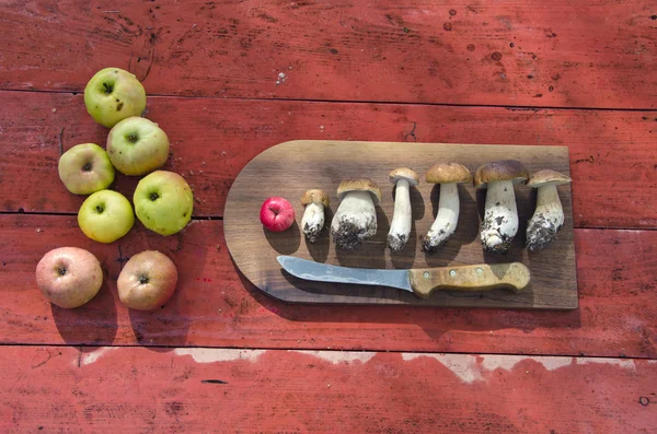 Placa de corte de cozinha com cogumelos e maçãs na mesa — Fotografia de Stock