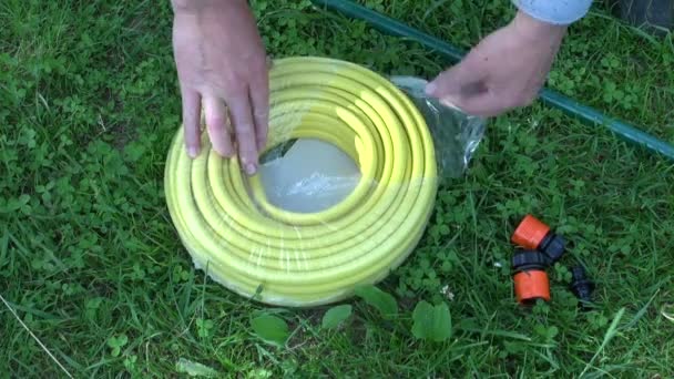 Dos manos desplegando nueva manguera de agua en el prado — Vídeo de stock