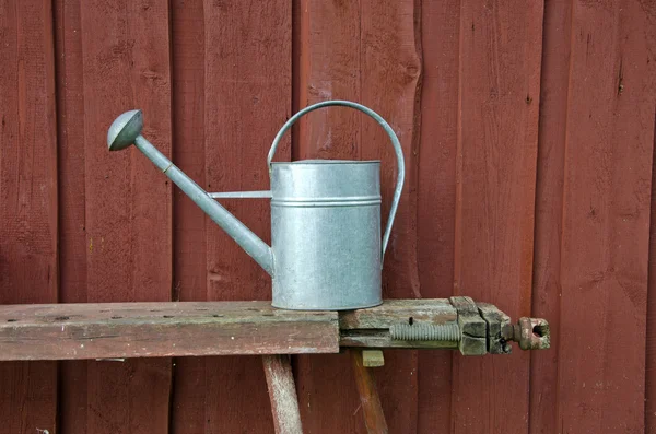 Metalen gieter op Bank naast rode houten muur — Stockfoto