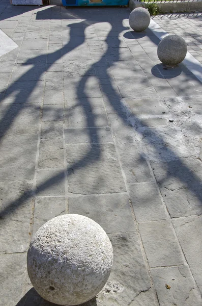 Baumschatten auf Straßenpflaster mit runden dekorativen Steinkugeln — Stockfoto