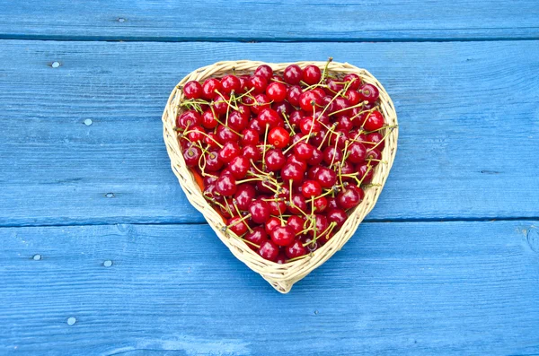 Heart shaped wicker basket full of cherries on blue background — Stock Photo, Image