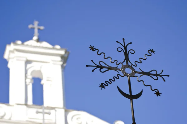 Close-up van black metal kruis met een witte kerk in de achtergrond — Stockfoto