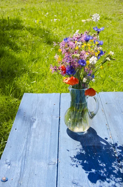 Wildfowers ve skleněné konvici na modrém stole — Stock fotografie