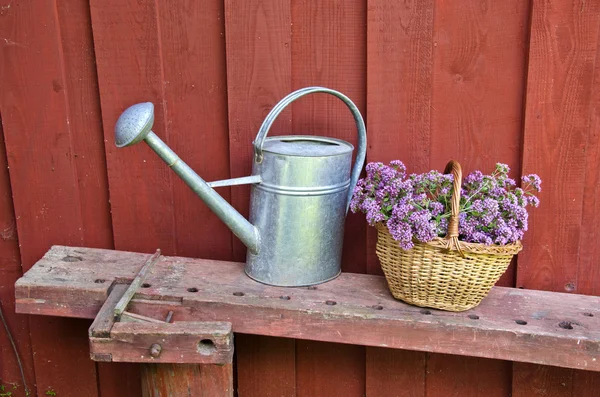 Metalen gieter en rieten mand door de houten muur — Stockfoto