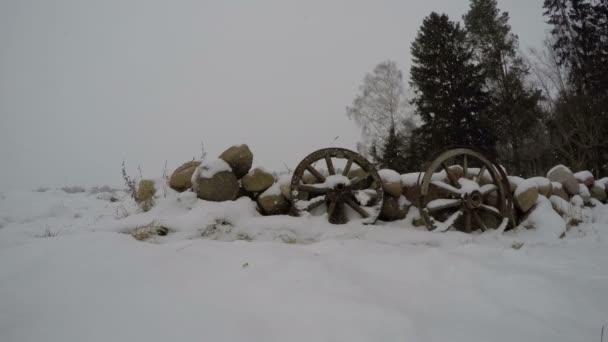 Dos ruedas de madera antiguas en la nieve por la pared de piedras, lapso de tiempo 4K — Vídeo de stock