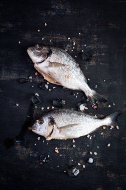 Koyu arkaplanda tuz ve buz ile taze çiğ dorada