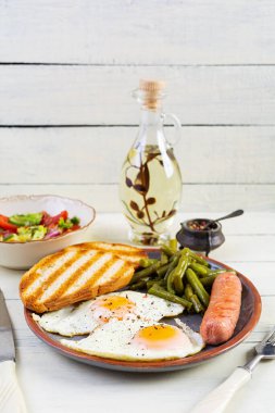 Yumurtalı kahvaltı, ızgara sosis, yeşil fasulye ve ahşap arka planda kızarmış ekmek.