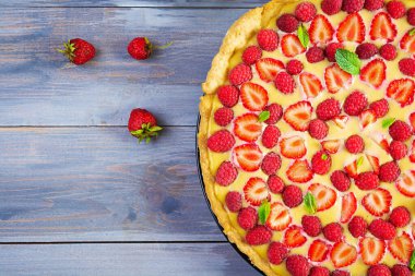 Ahşap zemin üzerinde çilek ve ahududu süslenmiş nane yapraklı nefis ev yapımı tart. Üst görünüm