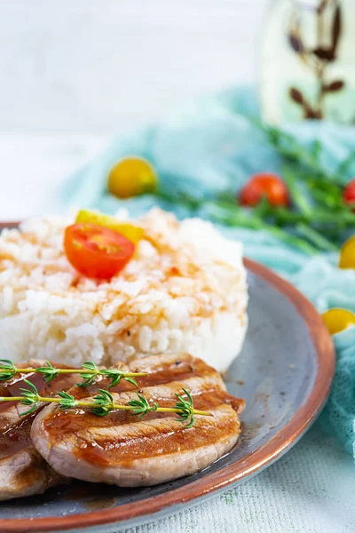 Izgara domuz etli pilav, domates ve beyaz arka planda yeşil otlar.