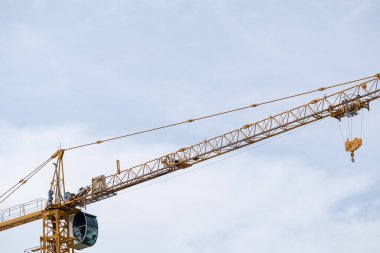 Long boom of the high tower crane with the hook is working in the construction site under the blue sky, development project in the urban area, front view with the copy space.