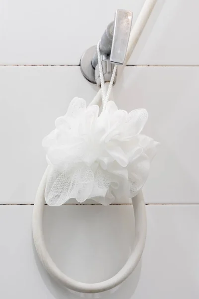 バスルームの白いタイルの壁の近くのシャワーバルブには 白いバスふわふわにぶら下がっている 体の皮膚をこすりつけるための清潔で柔らかいタッチ コピースペースのフロントビュー — ストック写真