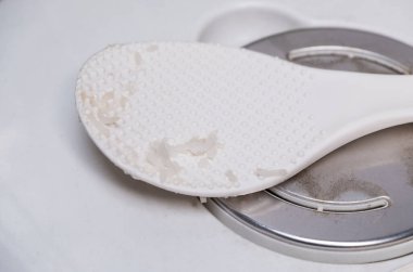 Plastik beyaz pirinç kepçesinin seçici odağı kuru pirinç kepçesiyle birlikte. Şehir evindeki elektrikli pirinç fırınının kapağında kullanıldıktan sonra, fotokopi alanı için önden görüş..