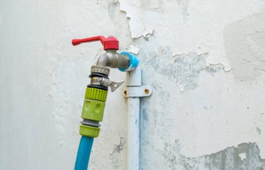 Kentin beyaz duvarının yanındaki bahçede kullanmak için hortuma bağlanan pirinç musluk, fotokopi alanının önü..