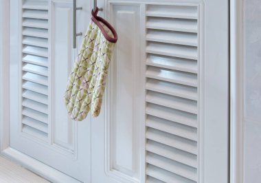 Yaprak desenindeki ısıya dayanıklı eldivenler mutfaktaki tezgahın altındaki dolabın sapında asılı..