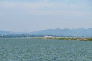 Dağ sıraları arasındaki düzlüklerde bulunan büyük rezervuarın baraj sırtındaki asfalt yol manzarası, fotokopi alanı için ön manzara.