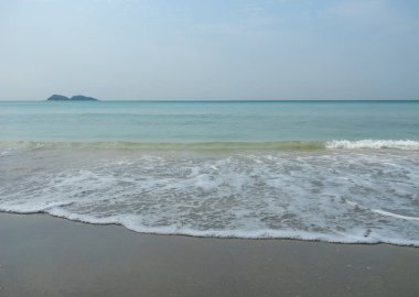 Yumuşak beyaz dalga köpüğü sakin bir sabahta boş, sakin bir plaja vurur. Seyahat ve rahatlama kavramları için ideal deniz manzarası arkaplanı.