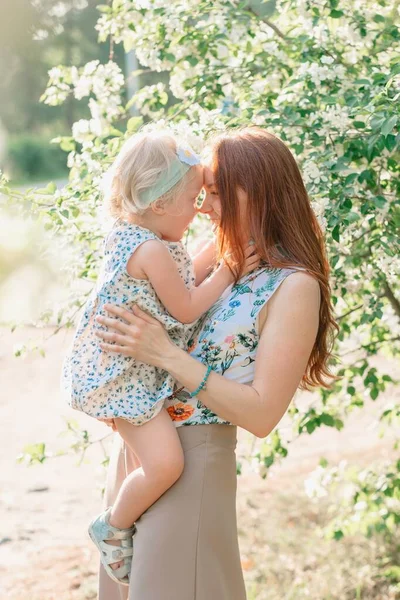 Mother touching nose with happy daughter in a blooming apple orchard — Stock Photo, Image