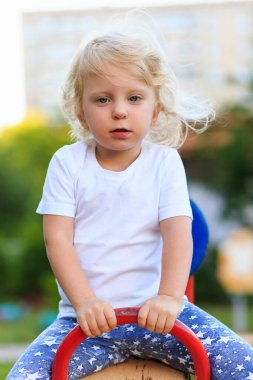 Little three years old child riding on the teeter at playground. Kid playing outdoor.