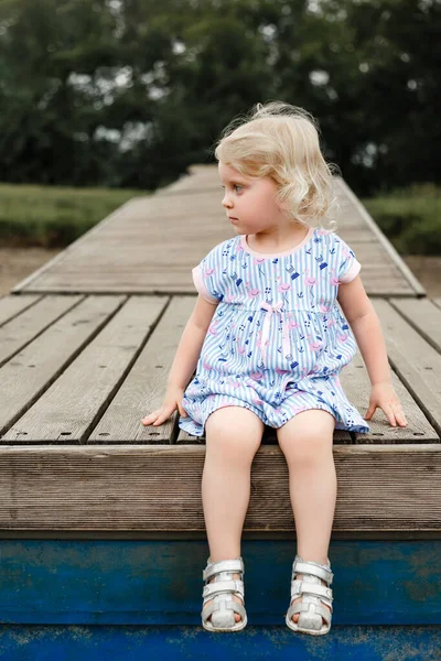 Retrato de uma linda garota loira sentada em uma pantone de madeira. — Fotografia de Stock