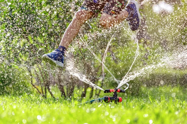 Kind springt über Gartenbewässerungsregner — Stockfoto