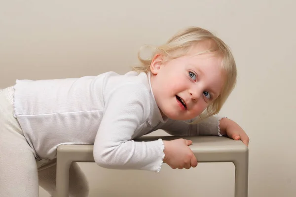 Portrait of a funny two-year-old smiling girl lying on a stepladder stool — Stock Photo, Image