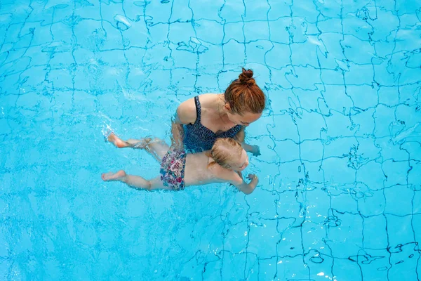 Szczęśliwa rodzina. Mama uczy córkę pływać w basenie w wieku 2-3 lat. Widok z góry. — Zdjęcie stockowe