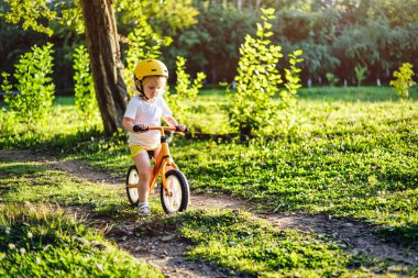 Küçük sevimli beyaz kız egzersiz yaparken eğleniyor. Park Ormanı 'nda motosiklet sürüyor.. 