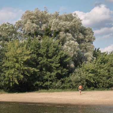 Bir adam ve ağaç, tek bir adam yüzme şortuyla sudan çıkar.