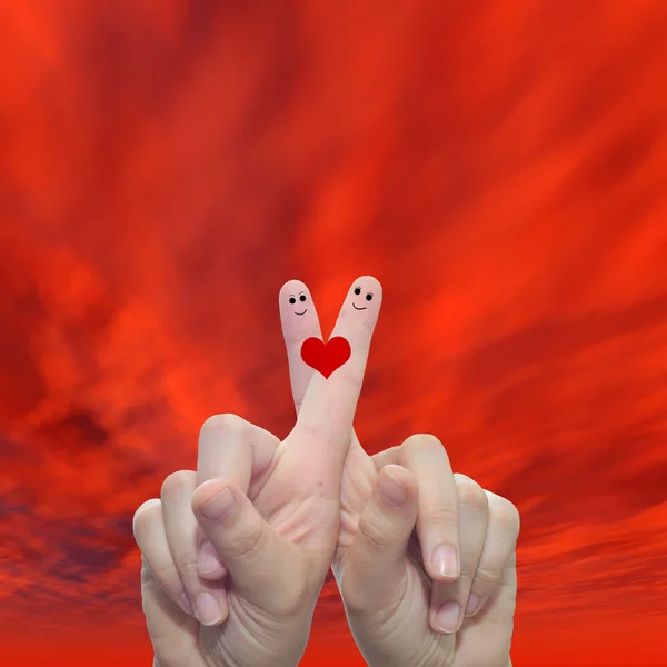 hands with two fingers painted with a red heart