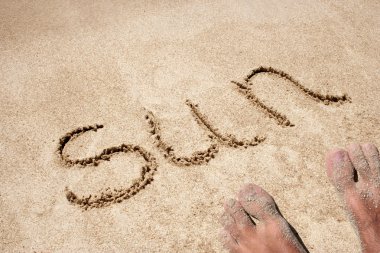Concept or conceptual sun text handwritten in sand on a beach with feet in an exotic island for tropical