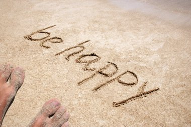 Concept or conceptual Be happy text handwritten in sand on a beach with feet in an exotic island for tropical