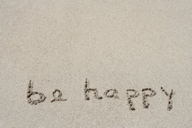 Concept or conceptual Be happy text handwritten in sand on a beach with feet in an exotic island for tropical