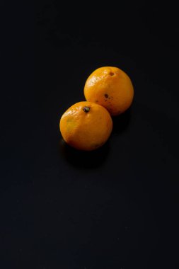 Koyu bir arka planda iki olgun mandalina. Derilerinde doğal koyu lekeler var. Bu da organik ve sağlıklı olduklarının kanıtı. Üzerlerinde GDO kimyasalları kullanılmamış..