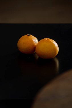 Koyu bir arka planda iki olgun mandalina. Derilerinde doğal koyu lekeler var. Bu da organik ve sağlıklı olduklarının kanıtı. Üzerlerinde GDO kimyasalları kullanılmamış..