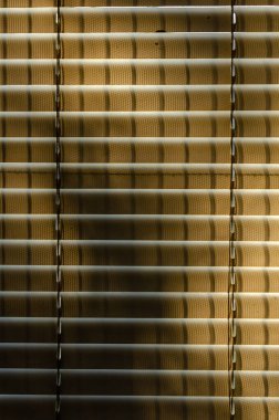 Pencere için Venedik panjurları, güneş ışığının içinden geçerek gölgelerle soyut şekiller oluşturur.