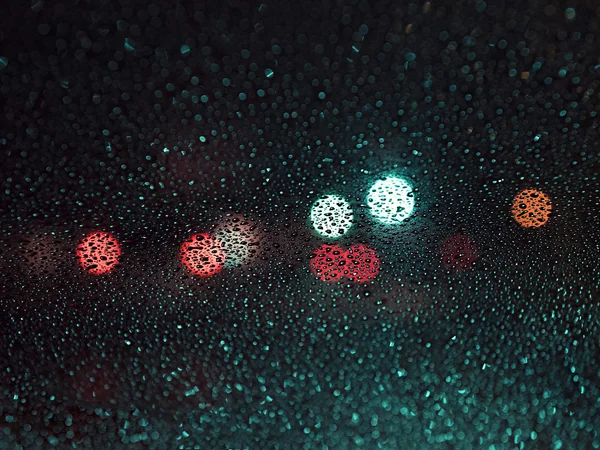 Gocce di pioggia sul vetro su sfondo sfocato di macchie colorate — Foto Stock