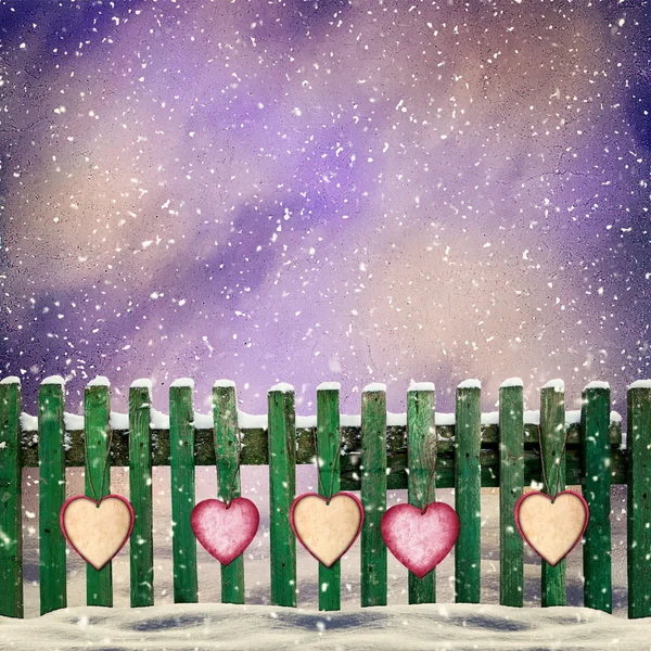 Snow-covered wooden fence with hanging on it with paper hearts — Stock Photo, Image