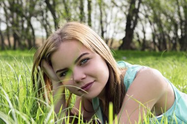 Genç şehvetli gülümseyen sarışın güneş ışığı altında çim üzerinde yalan