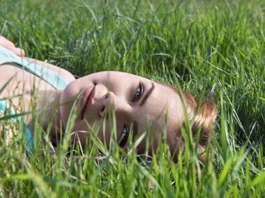 Genç şehvetli gülümseyen sarışın güneş ışığı altında çim üzerinde yalan