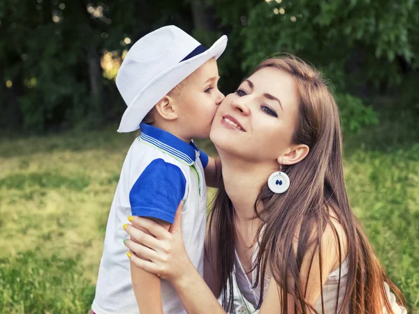 Boy kissing his mother on the cheek outdoors — Stock Photo, Image