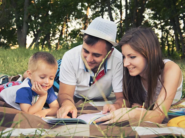 Parents with a child reading a book outdoors — Stock Photo, Image