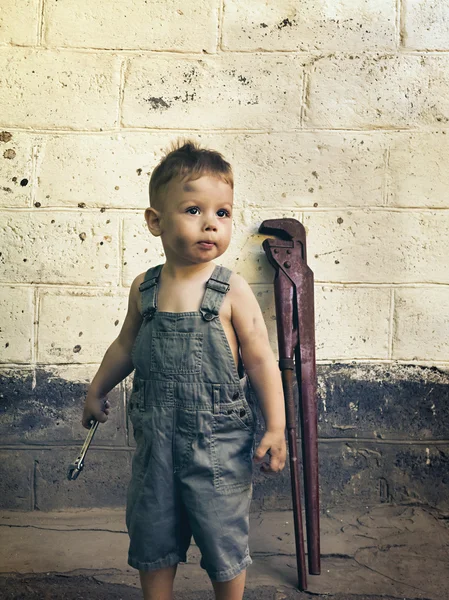 Pequeno menino com uma chave inglesa de pé na parede — Fotografia de Stock